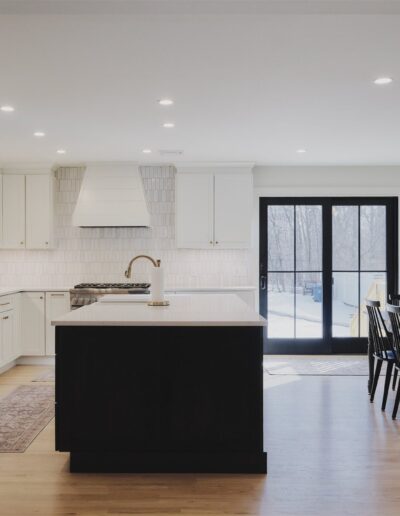 Modern kitchen with white cabinets, a central island, and adjacent dining area with black chairs. Large glass doors open to an outdoor view.