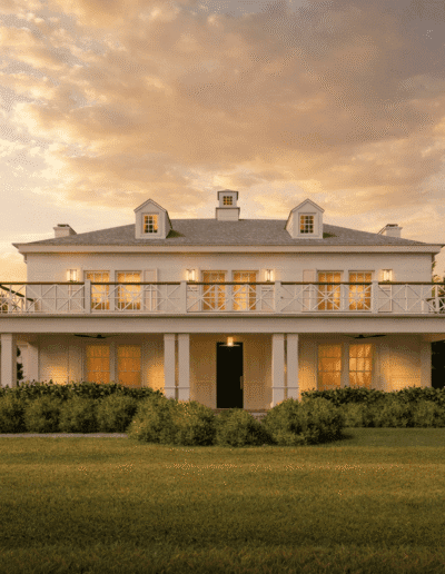 Two-story white colonial-style house with a large balcony, illuminated windows, and surrounded by greenery at sunset.